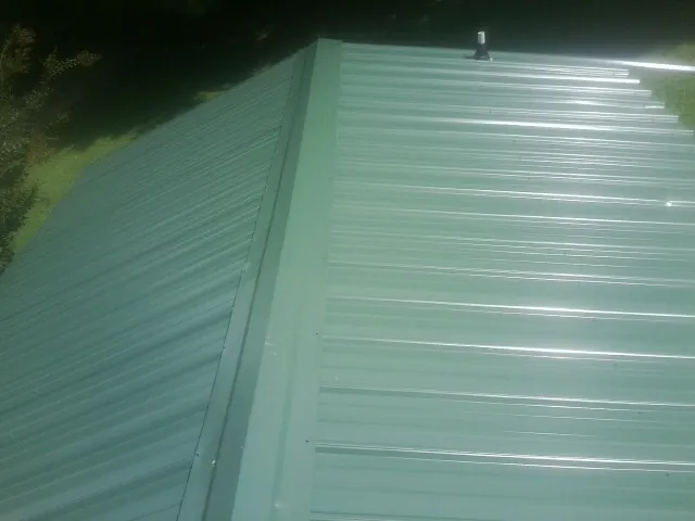 New green metal panels meeting at the ridge of a roof — Flat Roof Repair work by our crew in Portland